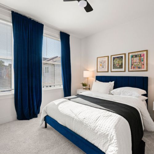 Bedroom 2 - An inviting bedroom with a navy upholstered headboard, ceiling fan, bedside lamps, and large windows. The stylish artwork adds a polished touch to the cozy space.