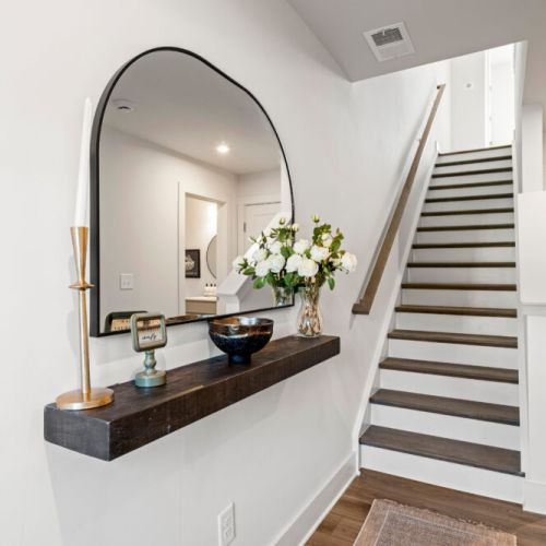 Bright entryway featuring a decorative console, oversized mirror, and staircase leading to the upper level. The thoughtfully styled space creates a welcoming first impression.