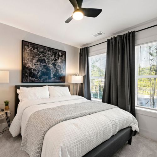 Bedroom 1 - a queen-size bed, ceiling fan, bedside tables, and large windows with blinds and curtains. A peaceful space to relax and recharge.