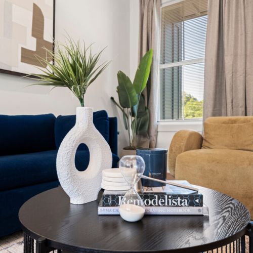 Bright living room with a plush navy sofa, cozy accent chair, and large windows that fill the space with natural light. The stylish coffee table and modern décor create a welcoming place to relax.