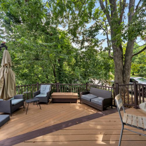 On the left, a wicker or woven outdoor sofa with dark grey cushions is placed along the railing
