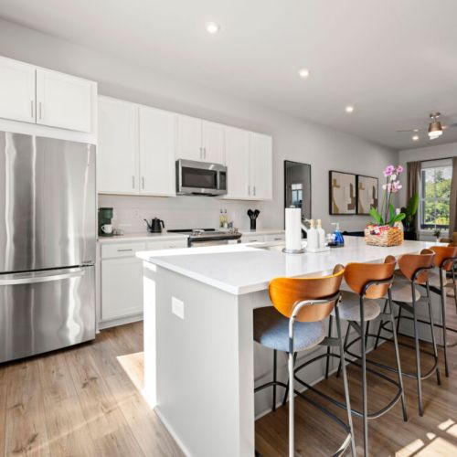 Open kitchen with a large quartz island and four bar stools, creating a convenient spot for casual meals or morning coffee. Stainless-steel refrigerator and modern appliances complete the space.