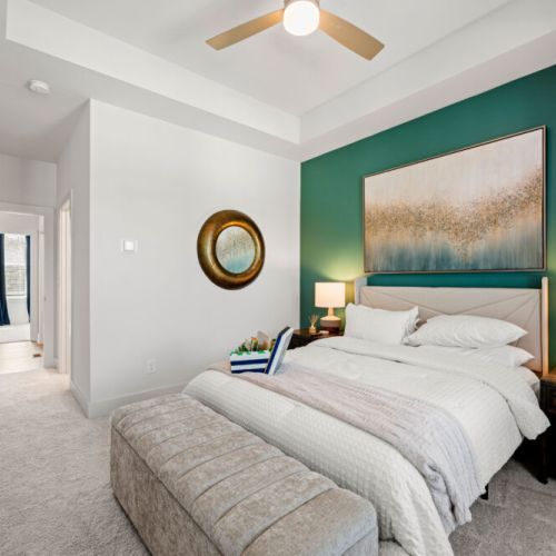 Bedroom 1 - Queen bed, stylish green accent wall, bedside lamps, and ceiling fan. A large upholstered bench provides convenient seating at the foot of the bed.