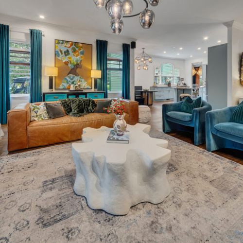 a cognac leather sofa, and bold teal velvet accents, all under a striking globe chandelier.