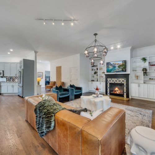 : A large, contemporary camel-colored leather sofa anchors the right side of the main seating arrangement