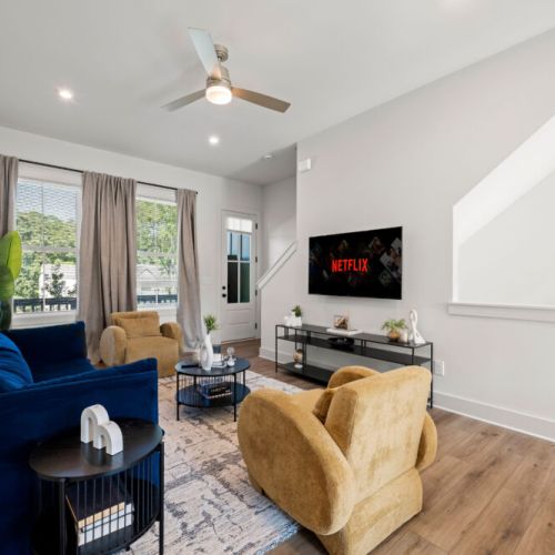 Spacious living area featuring a wall-mounted Smart TV, comfortable seating, ceiling fan, and oversized windows. A perfect spot for movie nights or unwinding after a day of exploring.