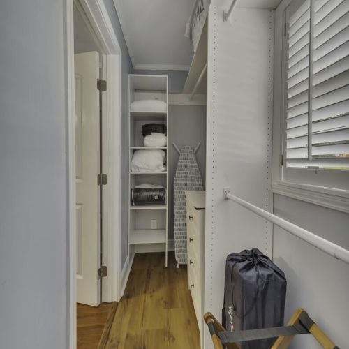 Walk-in closet containing: Extra bedding and pillows. Iron + ironing board and, organized shelving and storage