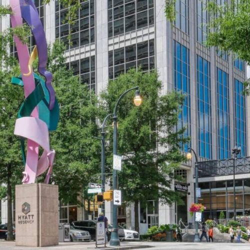 A tall, abstract sculpture stands prominently in the foreground on a stone pedestal